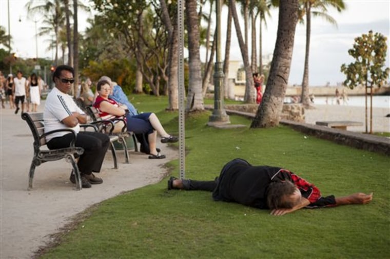 As tourists watch the sun go down, a man sleeps near Waikiki Beach on May 13, 2011 in Honolulu. 